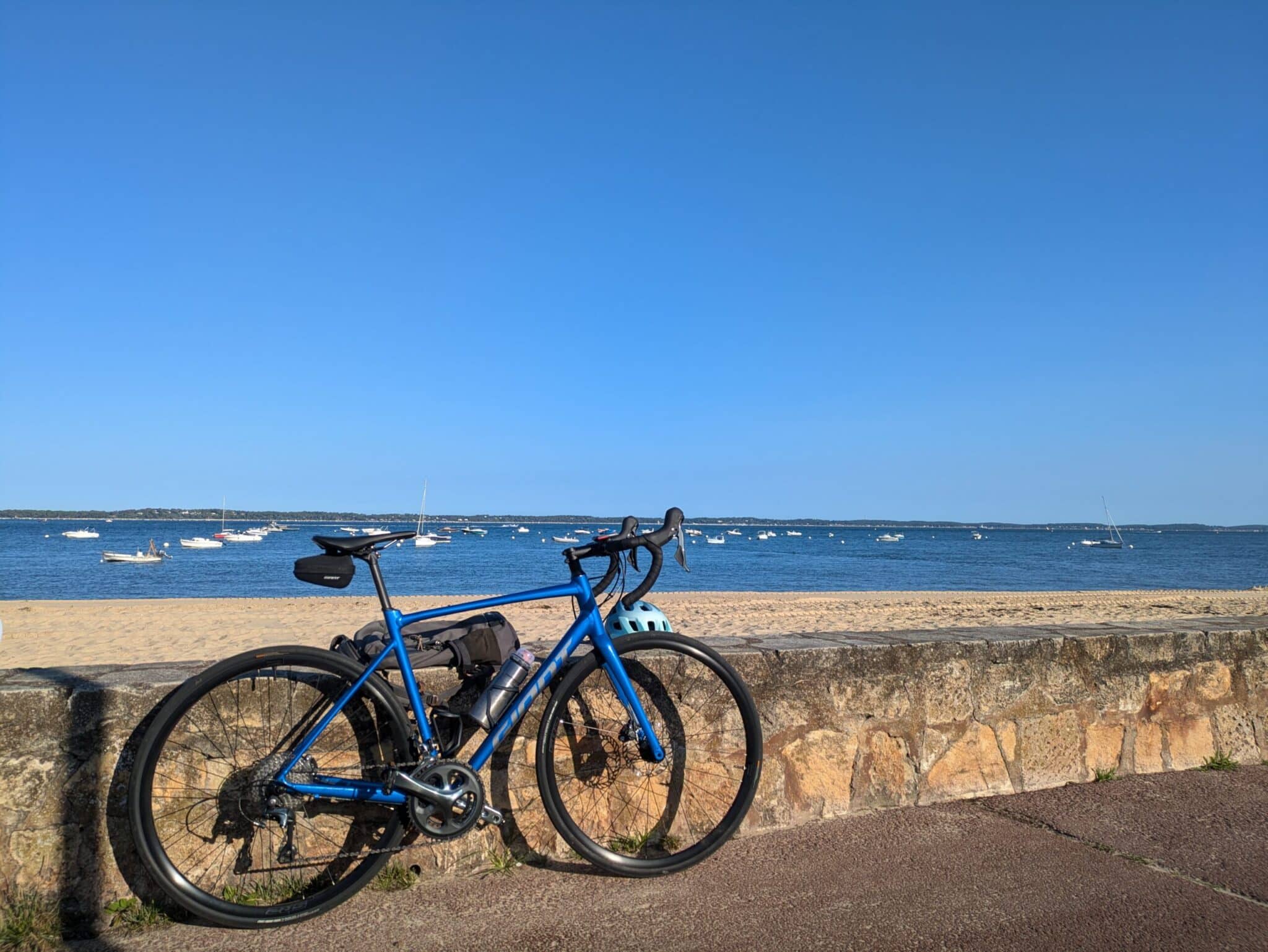 Vélo de route bleu avec sacoches sur une plage face au bassin, idéal pour la randonnée cyclotourisme